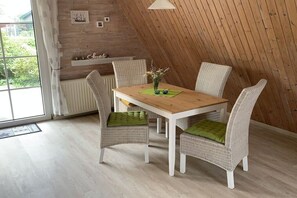 A dining area with a wooden table and wicker chairs, a radiator, and a view through a window. - Holiday home with 2 bedrooms (Spieka-Neufeld (Wurster Nordseeküste))