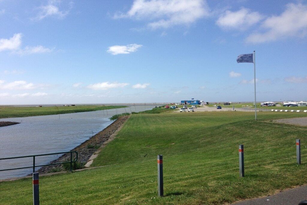 A grassy area with a flagpole, a water body, and a distant building.