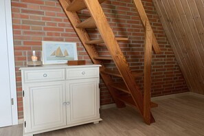 A white cabinet with drawers, a wooden ladder against a brick wall, and a framed picture on the cabinet. - Holiday home with 2 bedrooms (Spieka-Neufeld (Wurster Nordseeküste))