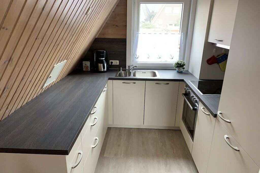 Una cocina compacta con encimera oscura, armarios blancos, horno empotrado y ventana que proporciona luz natural.