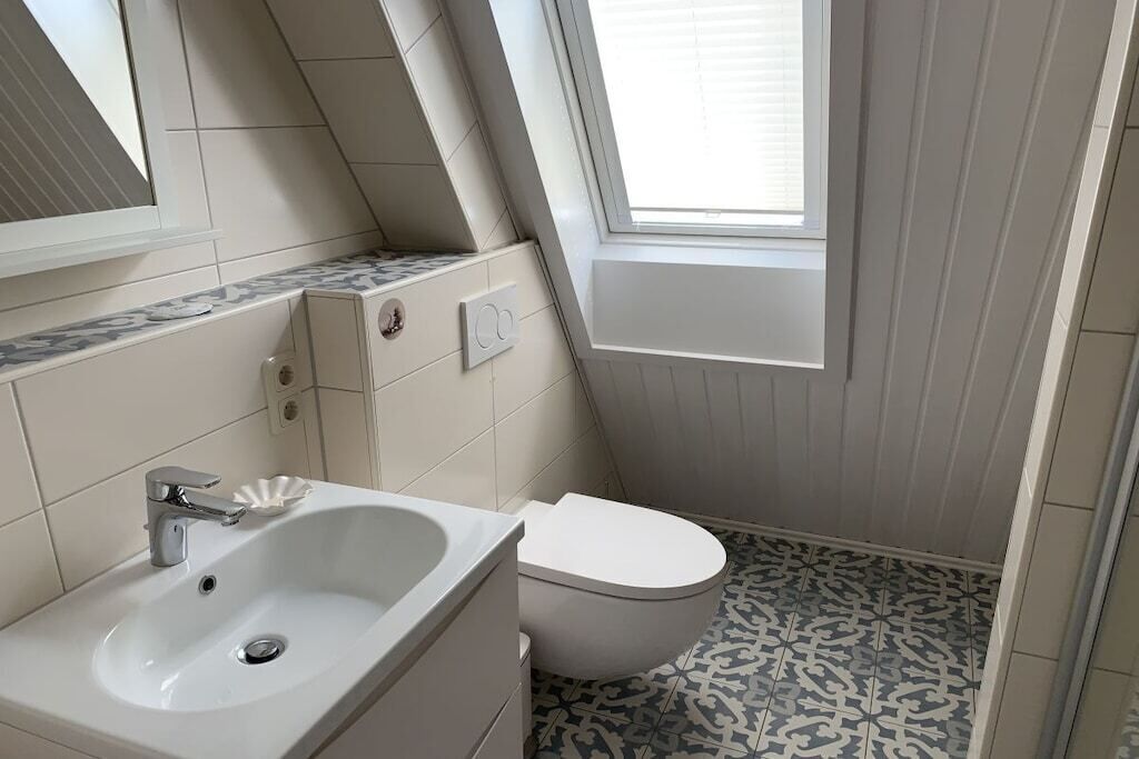 A small, modern bathroom with a white sink, toilet, and a window providing natural light.