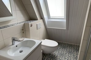 A small, modern bathroom with a white sink, toilet, and a window providing natural light. - Holiday home with 2 bedrooms (Spieka-Neufeld (Wurster Nordseeküste))