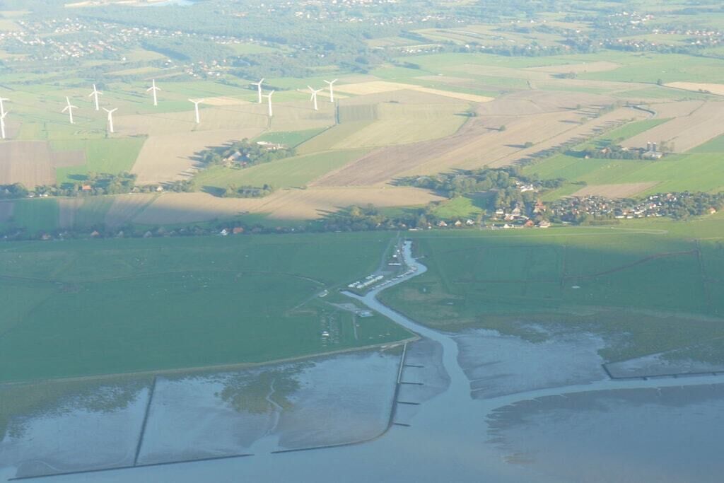 Vista aérea de un paisaje con aerogeneradores, un río y un pequeño asentamiento.
