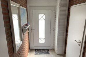 A hallway with a white door, a window with a cross pattern, and a door with a louvered design. - Holiday home with 2 bedrooms (Spieka-Neufeld (Wurster Nordseeküste))