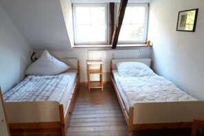 Ett sovsalsrum med två enkelsängar, en trästege och ett fönster med gardiner.