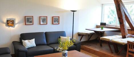 Una sala de estar acogedora con un sofá, una mesa de centro con un jarrón, y un comedor con una mesa y sillas.