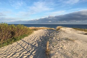 Un sentier de sable qui longe la plage et mène à l’océan, sous un ciel nuageux.
