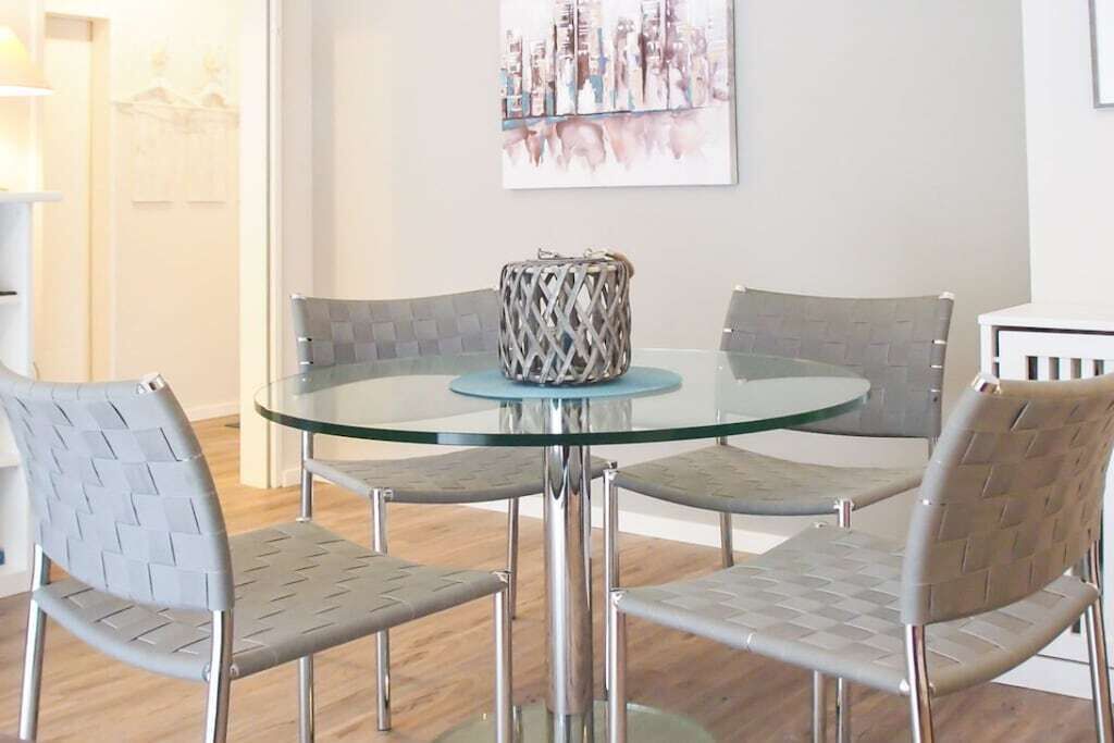 A dining area with a glass table surrounded by four chairs with woven backs.