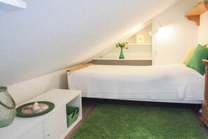 A small, cozy room with a bed, a green rug, a white dresser, and a small shelf with a vase. - Holiday apartment with 2 bedrooms (Timmendorfer Strand)