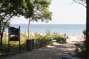 A beach path leading to the sea with a signboard, a trash bin, and people in the distance. - Holiday apartment with 2 bedrooms (Timmendorfer Strand)