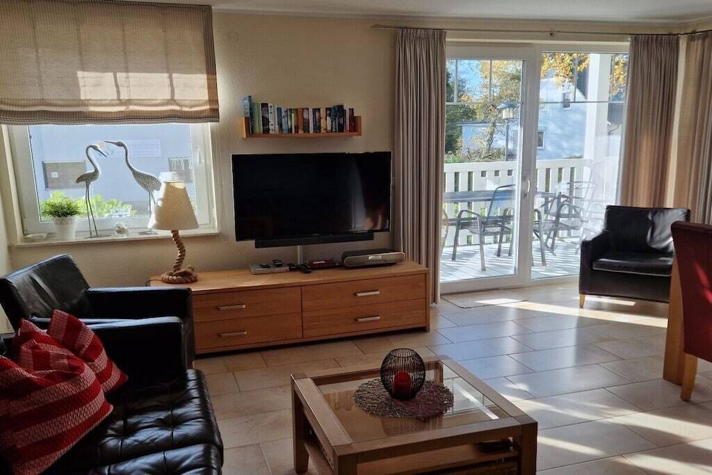 A living room with a television, a sofa, a coffee table, and a balcony with outdoor furniture.