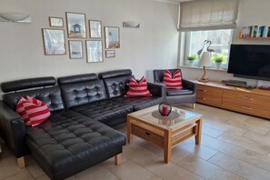 A living room with a black leather sofa, a wooden coffee table, and a television on a wooden cabinet. - Holiday apartment with 2 bedrooms (Heringsdorf)