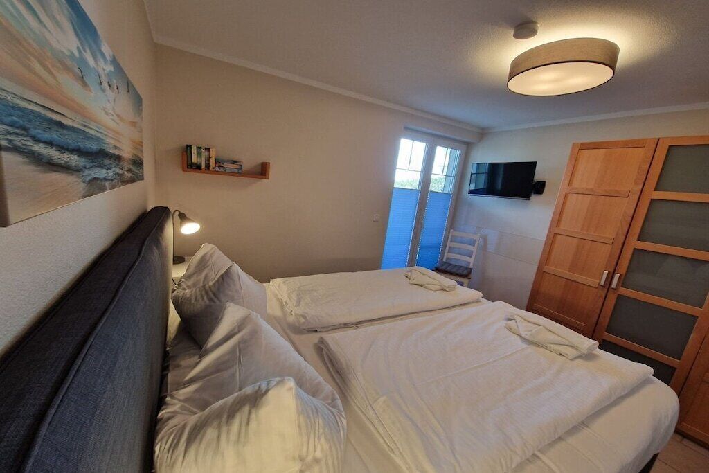 Un dormitorio con dos camas, una lámpara de techo, un televisor y una ventana.