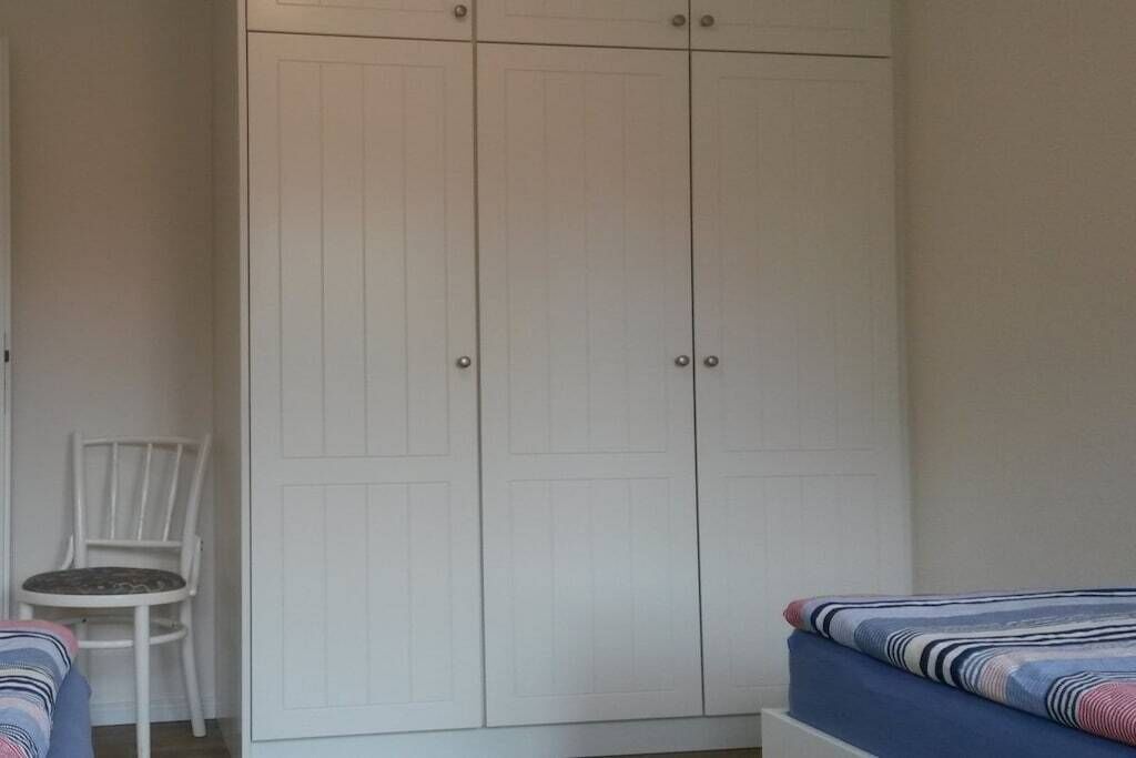A bedroom with a white wardrobe, a single bed with striped bedding, and a white chair.