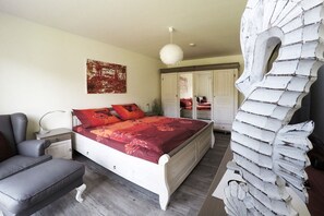 Ein Schlafzimmer mit einem Bett, Nachttischen, einem Sessel, einem Kleiderschrank und einer Wanddekoration.