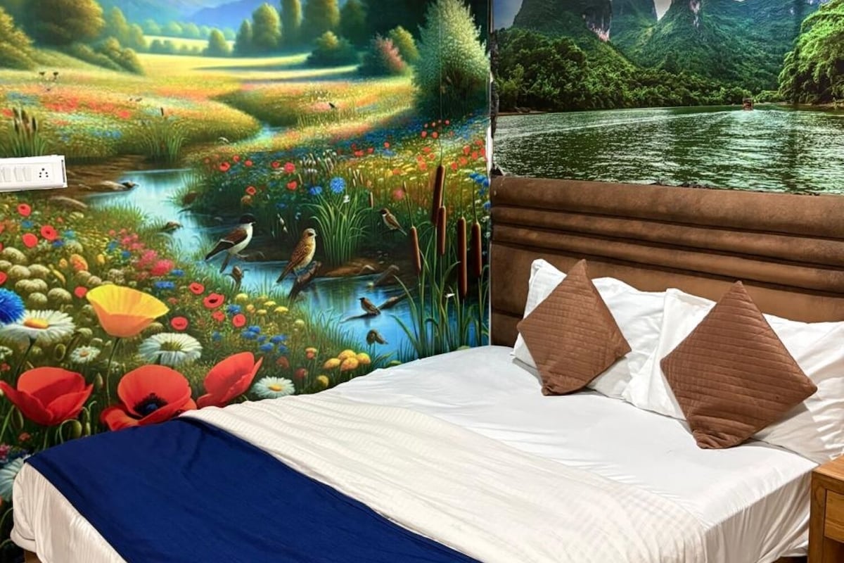 A bedroom with a mural of a landscape, a bed with white bedding and brown pillows, and a wooden headboard.