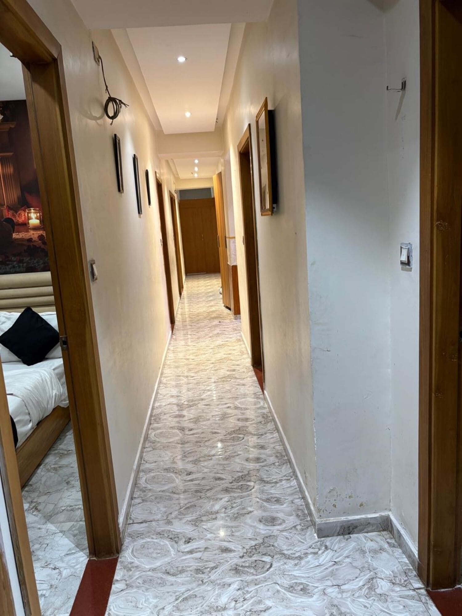 Ein Hotelgang mit Marmorboden, Holztüren und einem Bett auf der linken Seite.