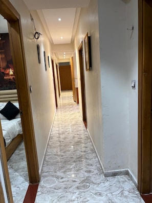A hotel hallway with a marble floor, wooden doors, and a bed visible on the left. - Hotel Sai Villa (Ahmedabad Gujarat)