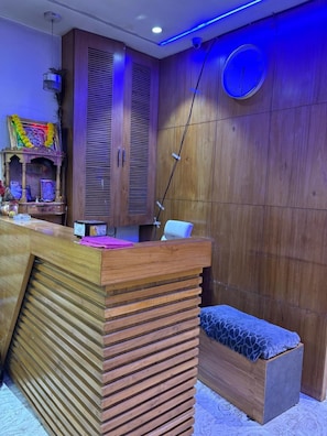A reception area with a wooden counter, a clock on the wall, and a bench. - Hotel Sai Villa (Ahmedabad Gujarat)