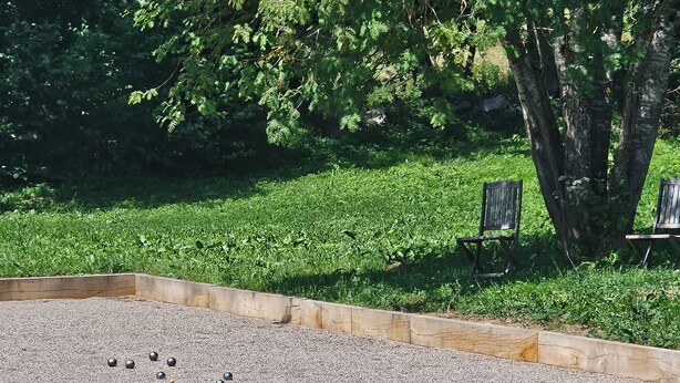 En trädgårdsdel med ett område med grus för lek, träkanter och två bänkar under ett träd.