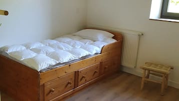 A small, single-bed room with a wooden bed frame and a small wooden stool.