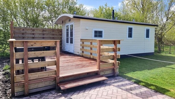 A small, single-story building with a wooden deck and a fenced entrance. - Beautiful pylon OK21 (Oostkapelle)