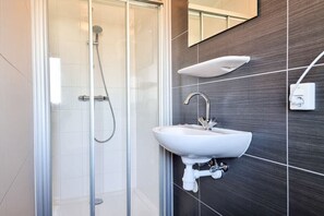 Ein modernes Badezimmer mit einer gläsernen Duschkabine, einem weißen Waschbecken und einer dunkel gefliesten Wand.