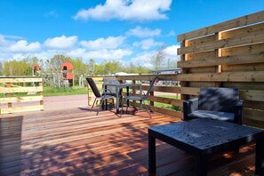 Eine Terrasse im Freien mit Tisch und Stühlen, umgeben von Holzzaun und blauem Himmel.