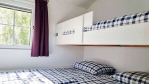 A room with a bunk bed, a window with curtains, and a bed with a checkered bedspread. - Beautiful pylon OK21 (Oostkapelle)