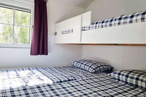 Ein Zimmer mit einem Etagenbett, einem Fenster mit Vorhängen und einem Bett mit kariertem Überwurf.