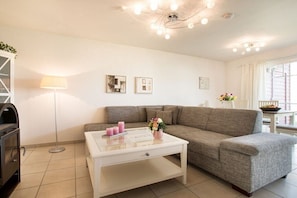 A living room with a sofa, a coffee table, a lamp, and a fireplace. - Strandnest Sierksdorf (Sierksdorf)