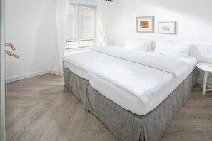 Ein Schlafzimmer mit einem Bett, einem Nachttisch, einem Fenster mit Vorhängen und einer Wand mit zwei gerahmten Bildern.