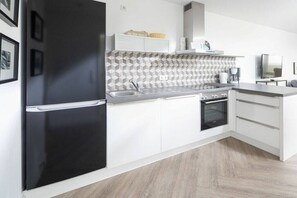 A modern kitchen with a black refrigerator, white cabinets, a tiled backsplash, and a built-in oven. - Oystercatchers in house Bill15 (Juist)
