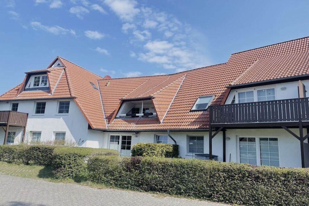 A two-story residential building with a red-tiled roof, multiple windows, and a balcony.