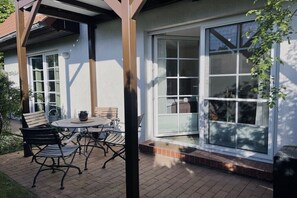 A patio with a table and chairs, a covered seating area, and a sliding glass door leading to a covered porch. - Holiday apartment with 1 bedroom (Dierhagen)