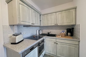 A kitchen with white cabinets, a toaster, a kettle, and a coffee maker on the countertop. - Holiday apartment with 1 bedroom (Dierhagen)