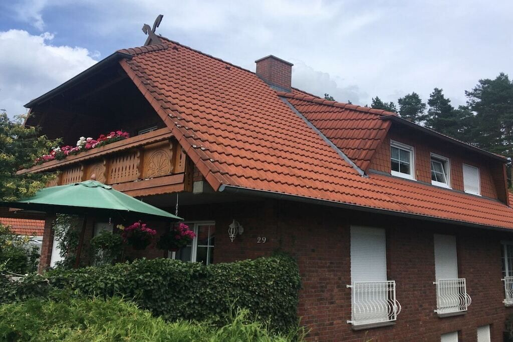 A two-story house with a sloped red-tiled roof, a balcony with flowers, and a green umbrella.