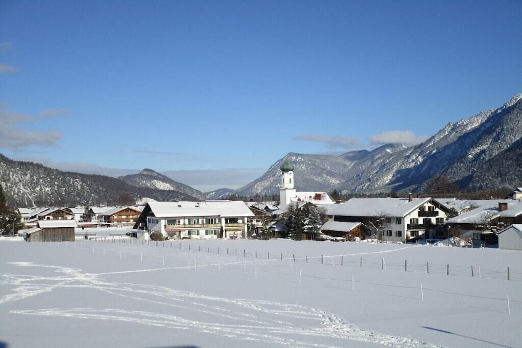 Ein verschneites Dorf mit Häusern, einer Kirche und Bergen im Hintergrund.