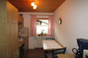 Eine kleine Küche mit Holzausstattung, einem Fenster mit rosa Vorhängen, einem Heizkörper und einem Tisch mit Stühlen.