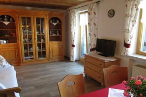 Una habitació amb armaris de fusta, una televisió, una taula de dinar amb cadires i una finestra amb cortines.