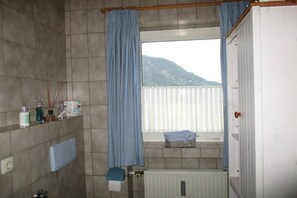 Een badkamer met een raam, een radiator en een plank met toiletartikelen.