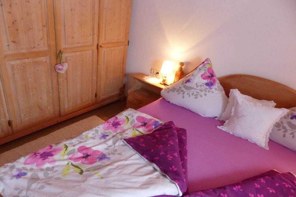 A bedroom with a bed, pillows, a nightstand, a lamp, and a wooden wardrobe.