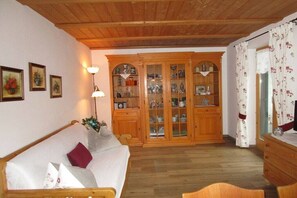 Ein gemütliches Zimmer mit Holzboden, einem weißen Sofa mit rotem Kissen, einem Holzschrank mit Glastüren und einer Lampe.