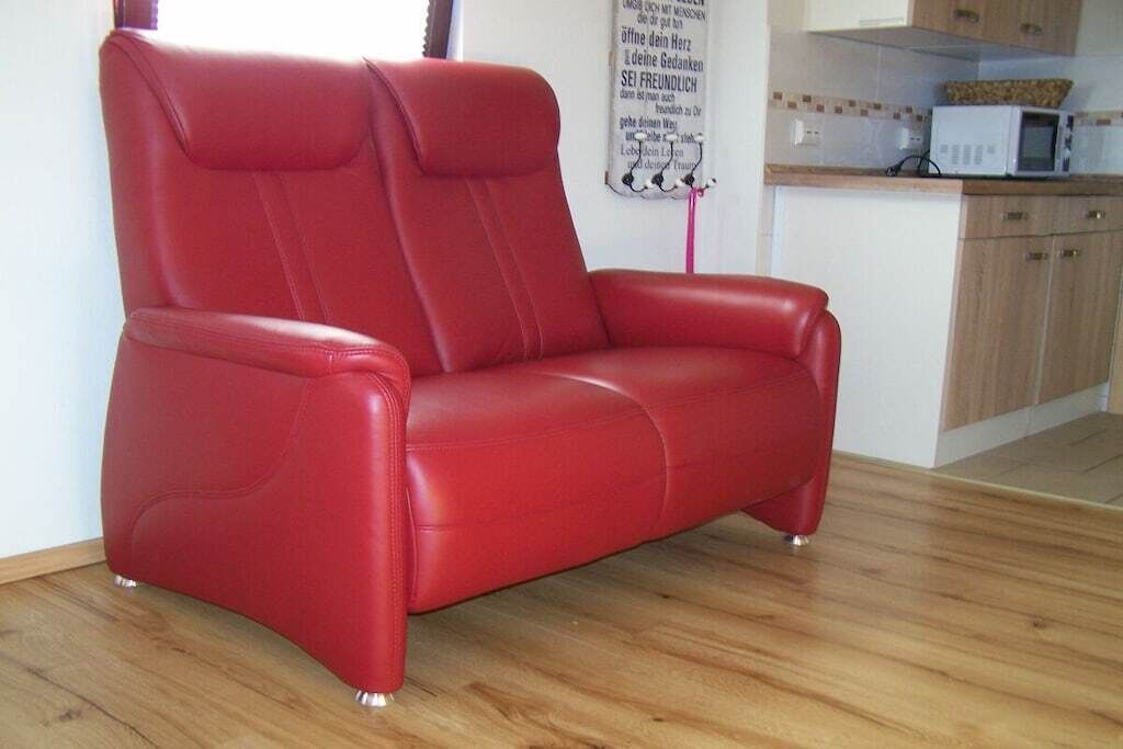 A red leather sofa in a room with wooden flooring and a kitchen area in the background.