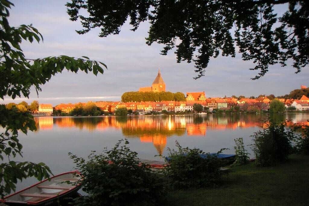 A calm lake with a church and residential buildings in the background.