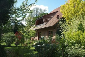 Ein Haus mit einem geneigten Dach, umgeben von üppigem Grün und Bäumen.