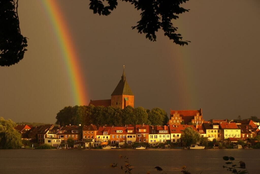 Eine Stadt mit einem markanten Kirchturm und einem Regenbogen über dem Wasser.