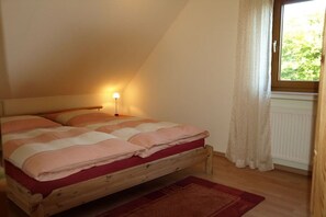Ein Schlafzimmer mit einem hölzernen Bett, einem Nachttisch mit Lampe, einem Fenster mit Vorhängen und einer Heizung.