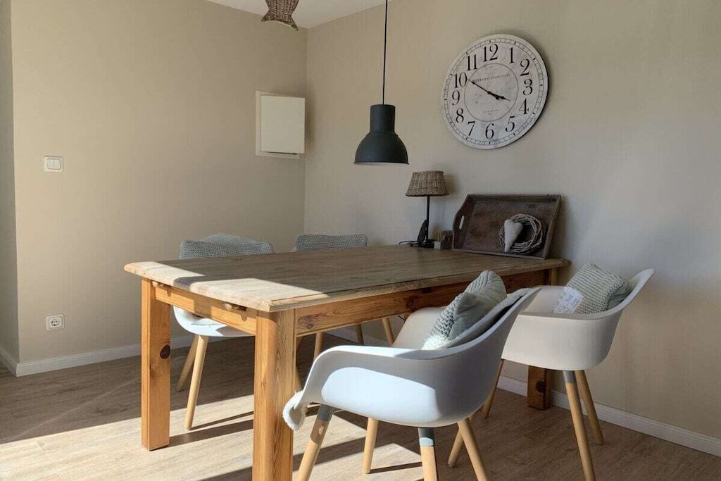 A dining area with a wooden table, four chairs, a wall clock, and a pendant light.