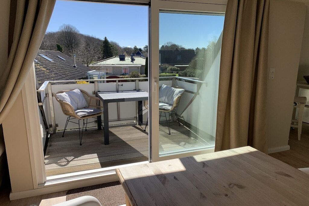 Un balcone con tavolo e sedie, una porta scorrevole in vetro e vista sul quartiere.